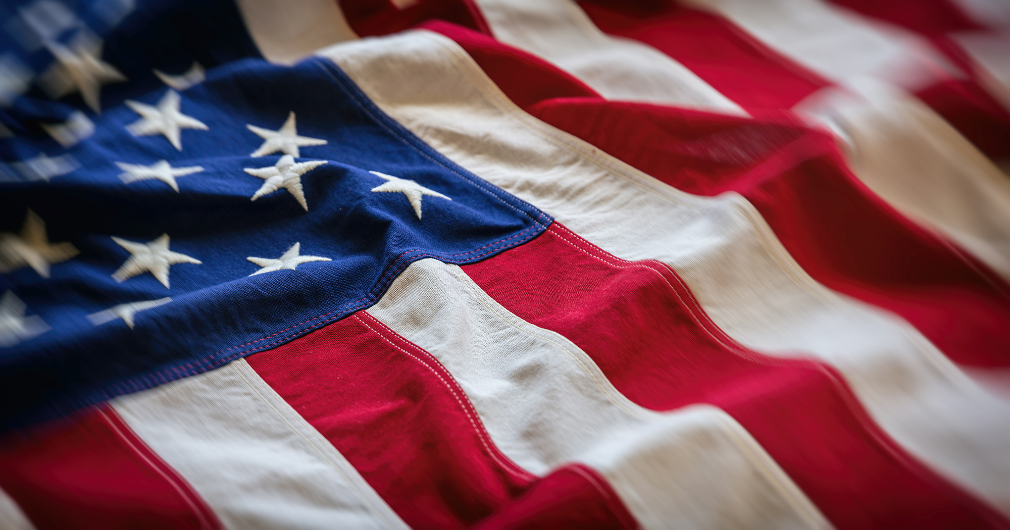american-flag-patriotic-background Close-up view of the United States flag with embroidered white stars on a blue field and red and white stripes flowing in soft waves.