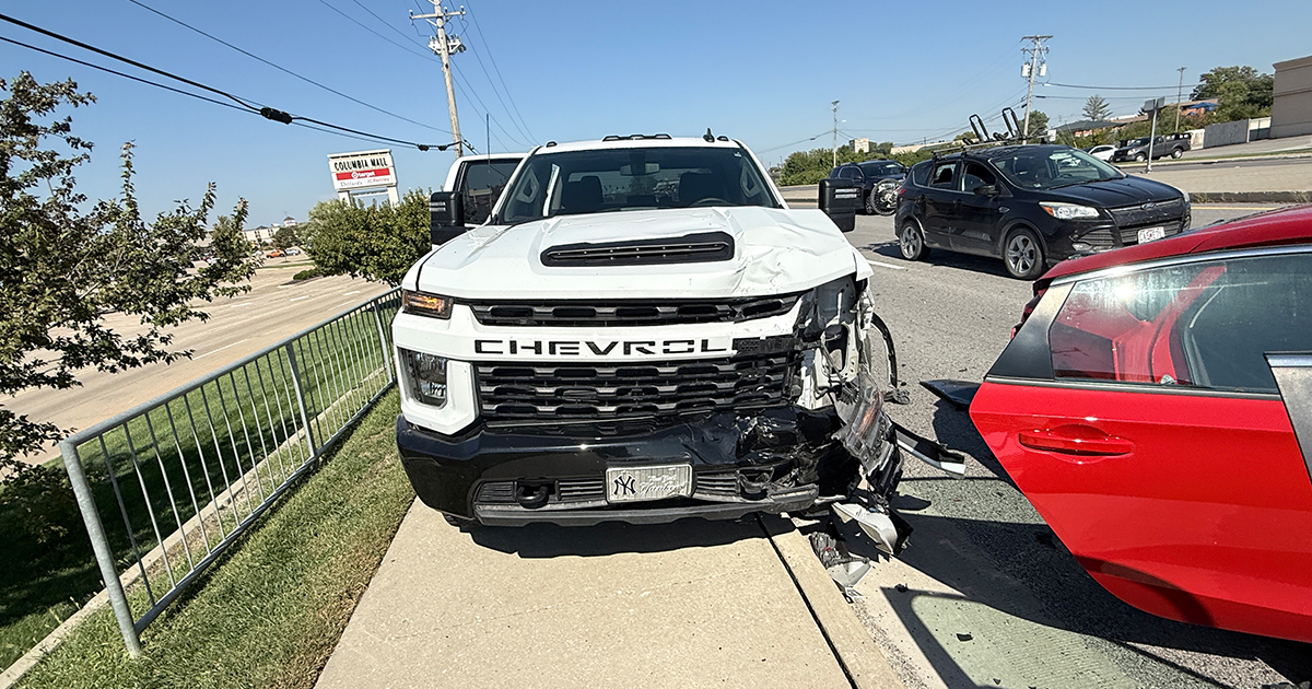 White commercial work truck with front-end damage parked beside a red Honda Civic after a multi-vehicle crash.