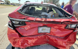 Rear view of a red Honda Civic with severe rear-end damage, shattered back glass, and crushed trunk after a multi-vehicle crash.