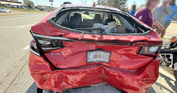 Rear view of a red Honda Civic with severe rear-end damage, shattered back glass, and crushed trunk after a multi-vehicle crash.